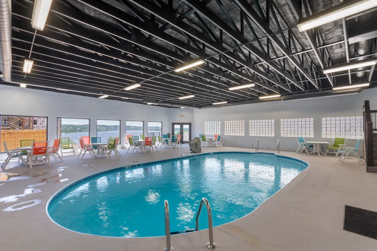 The image showcases a spacious indoor pool area filled with natural light from large windows, vibrant lounge chairs, and an inviting atmosphere for relaxation and group gatherings regardless of season.