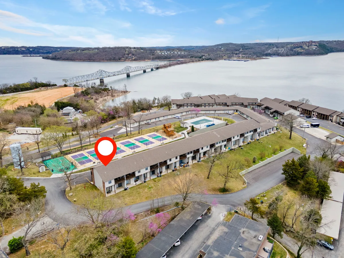 A vibrant exterior shot of the property’s amenities, featuring sparkling swimming pools, a playground, and a scenic river view with a picturesque bridge in the background. The area is well-maintained, inviting guests to relax, swim, play sports, or enjoy a picnic by the water. The overall atmosphere is lively yet peaceful, highlighting the resort-style recreational features available to guests.