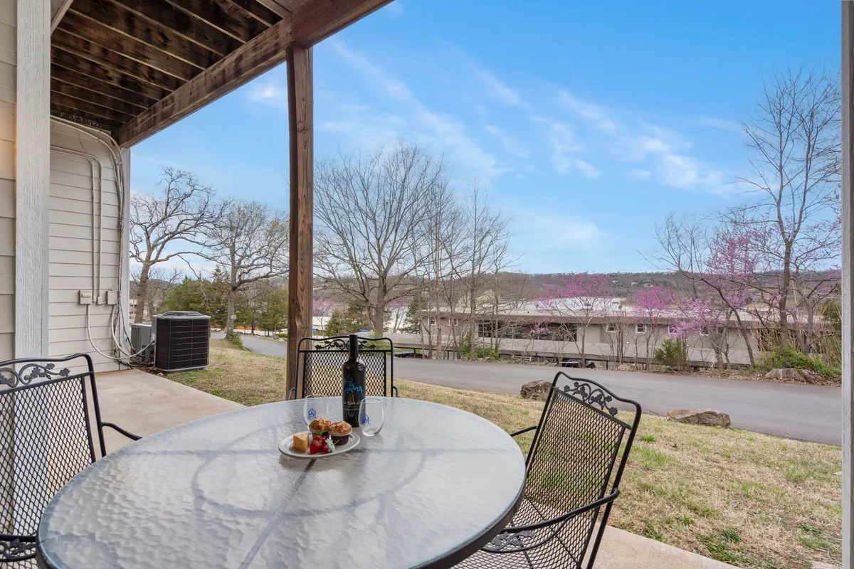 An inviting patio setup with a table set for outdoor dining, a bottle of wine, and glasses, surrounded by trees. The view suggests an intimate, private setting for enjoying coffee in the morning or sharing a romantic evening meal, with the soft natural light enhancing the cozy, serene mood.