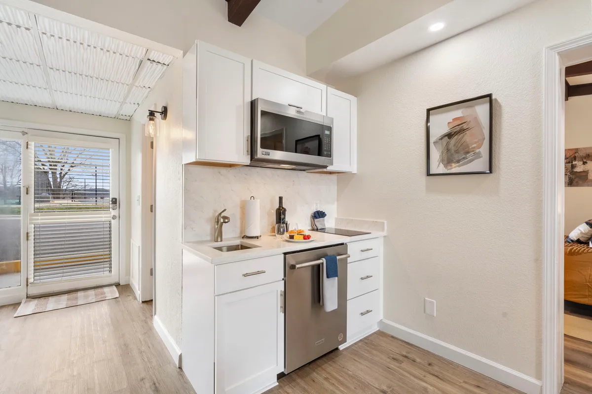 A modern kitchenette with sleek appliances, inviting artwork, and a well-lit, cozy atmosphere. The space invites cooking, entertaining, and enjoying time together as meals are prepared or shared.