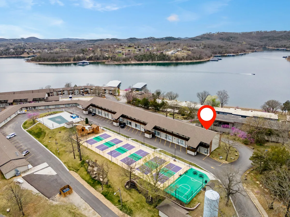 This exterior image captures a sweeping view of the property with a serene lake in the background, sports courts for tennis and basketball, and lush surrounding nature. The layout shows communal outdoor spaces, inviting friends to gather and be active together.