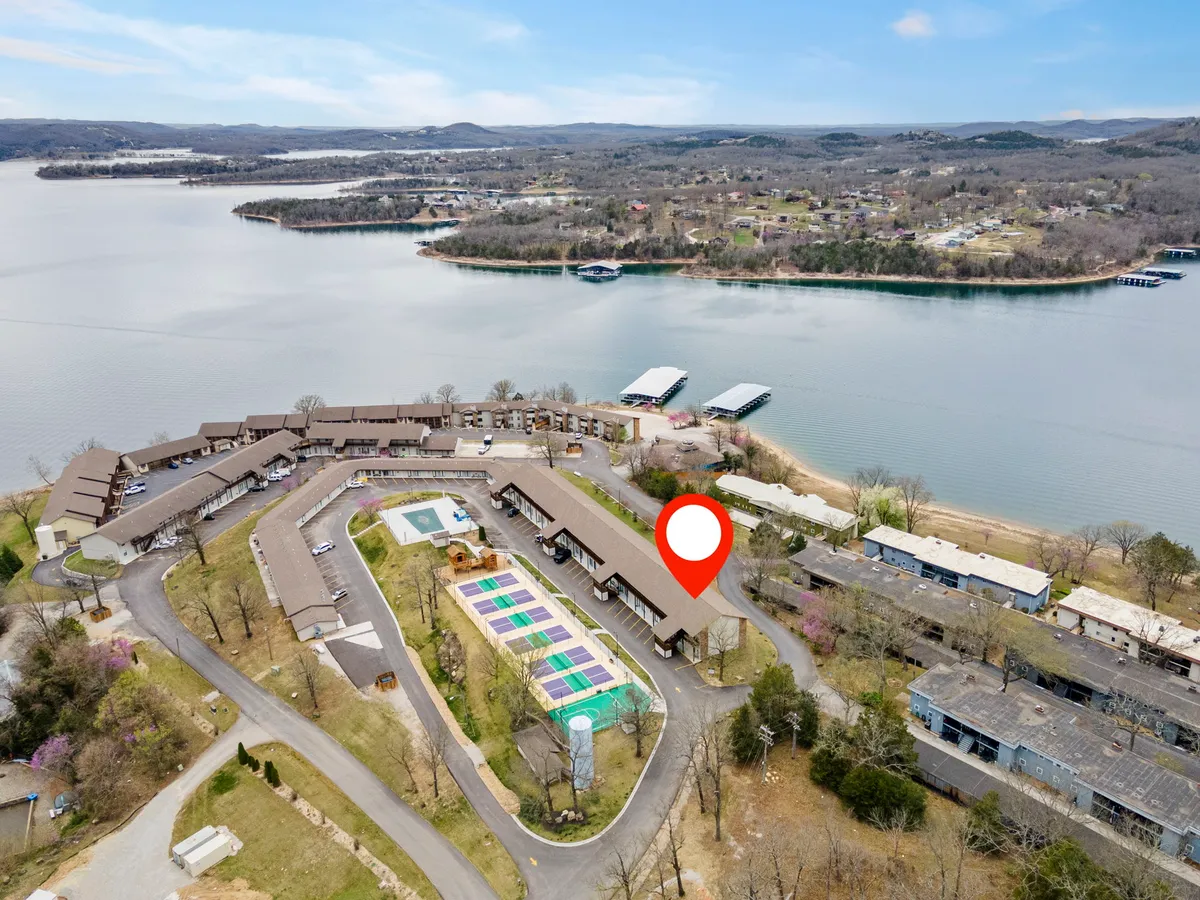 The photo showcases a tranquil lakeside setting with the lake and swimming pool prominently visible, surrounded by lush greenery and residential units. Families can be seen boating, swimming, and enjoying picnics along the water’s edge, emphasizing relaxation and outdoor adventure.
