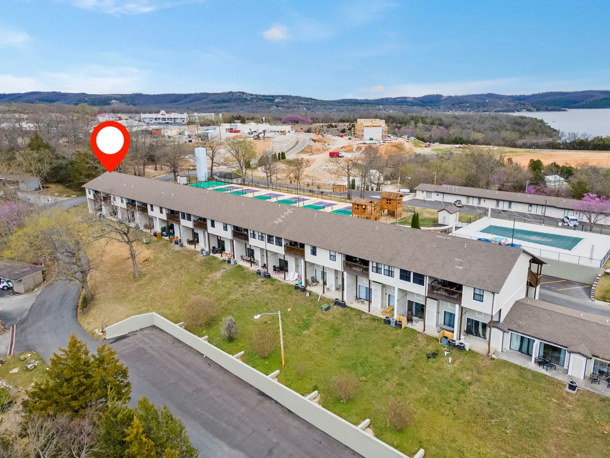 A tranquil exterior shot featuring the building's façade, a lush green lawn, the nearby lake shimmering in the background, and tall trees framing the scene. The setting evokes calm and offers a sense of privacy, perfect for couples seeking a nature escape.